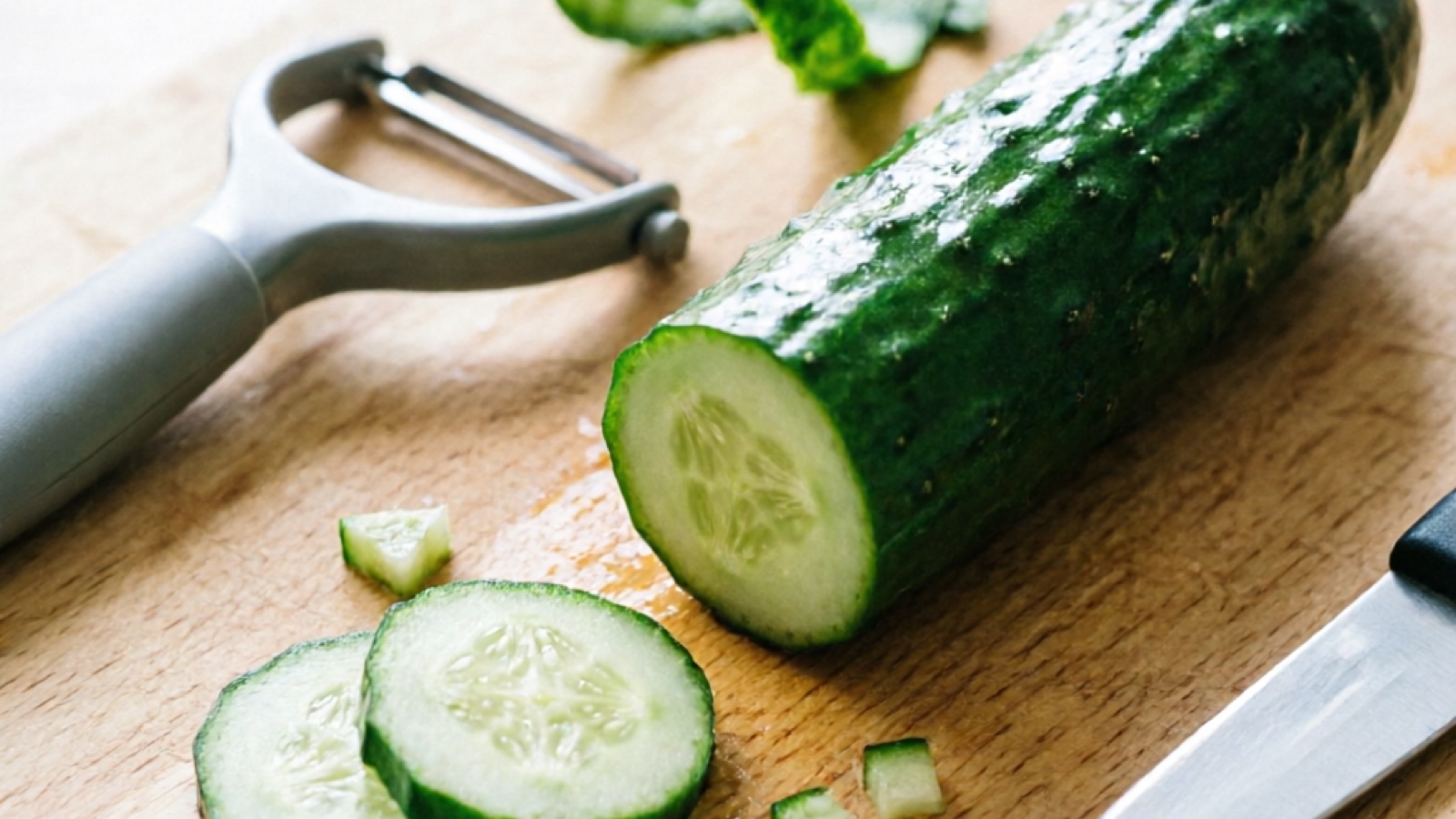 Washed cucumber being peeled and cut into hamster-sized pieces on a cutting board
